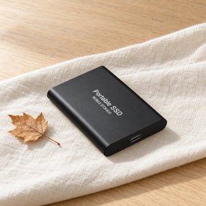 Zwarte externe SSD op linnen doek met esdoornblad